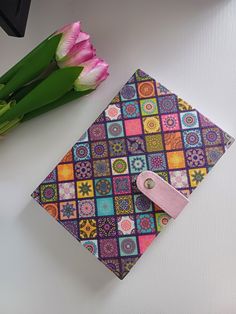 a colorful notebook with a pink tag on it sitting next to some tulips