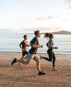 three people are running on the beach by the water and one person is wearing headphones