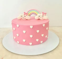 a pink cake with white hearts and rainbow on top