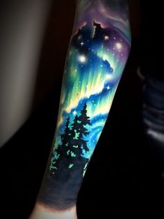 a man's arm with an aurora bore tattoo on it and trees in the foreground