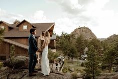 a bride and groom standing on top of a rock in front of a mountain lodge