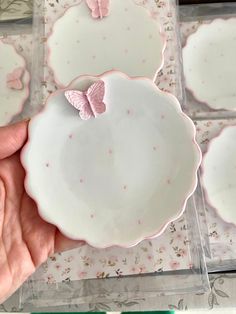 a hand holding a plate with pink butterflies on it and other plates in the background