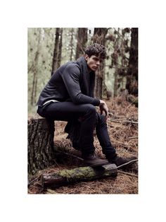 a young man sitting on top of a tree stump in the middle of a forest