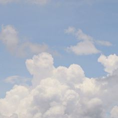 the airplane is flying high in the sky with white clouds behind it on a sunny day