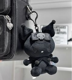 a black stuffed animal hanging from the side of a bag with a keychain attached to it