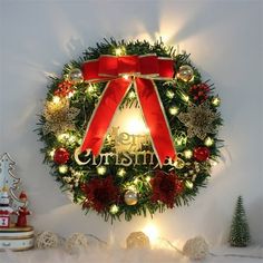 a christmas wreath on the wall with lights and ornaments around it, decorated with red ribbon