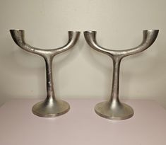 two silver candlesticks sitting on top of a pink table next to a white wall