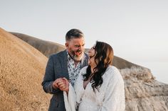 a man and woman standing next to each other on top of a hill near the ocean