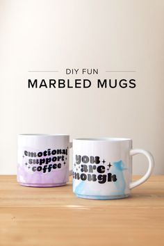 two coffee mugs sitting next to each other on top of a wooden table with the words, diy fun marbled mugs