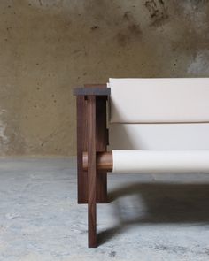 a wooden bench with white fabric on the armrests and back rests against a concrete wall