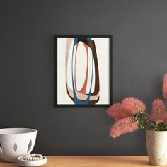 a vase filled with pink flowers sitting next to a painting on a wall above a wooden table