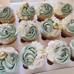 twelve cupcakes with blue frosting and gold decorations in a white cardboard box