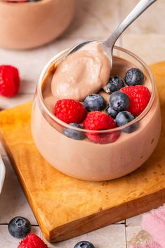 a spoon with some fruit in it on top of a wooden cutting board next to berries and yogurt