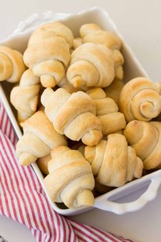 a white dish filled with rolls sitting on top of a red and white striped napkin