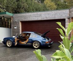 a blue car parked in front of a garage with its doors open and the door opened