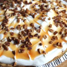 a pie with white frosting and pecans on top sitting on a wooden table