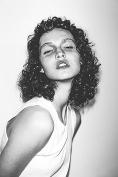 a black and white photo of a woman with curly hair looking at the camera while wearing a tank top