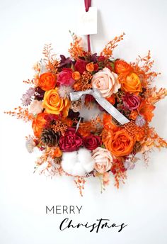 a christmas wreath with flowers on it and a merry sign hanging from the front door