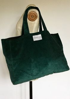 a green bag sitting on top of a wooden stand next to a white wall with a button in it