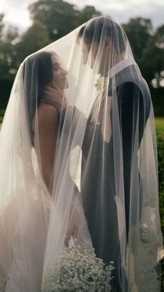 a bride and groom standing under a veil in front of some bushes with flowers on it