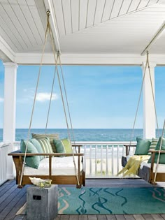 a porch swing with pillows on it next to the ocean and an area rug that looks like wood