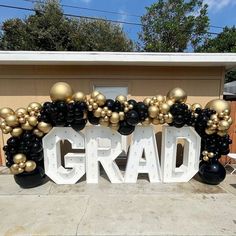 a large balloon arch that says grad with black and gold balloons