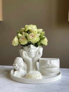 a white vase with flowers in it sitting on a table next to a cup and saucer