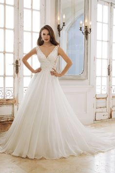 a woman in a white wedding dress standing next to a mirror with her hands on her hips