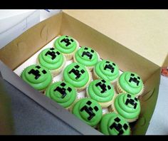 a box filled with green cupcakes covered in frosting and black icing