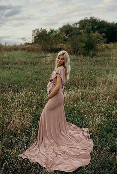 a pregnant woman in a pink dress standing in the grass with her hands on her hips