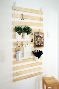 a wall mounted potting rack with hanging pots and utensils on it, next to a small wooden stool