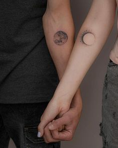 two people holding hands with the moon and half - moon tattoo on their arm,