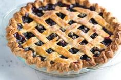 a blueberry pie sitting on top of a white table next to a glass bowl