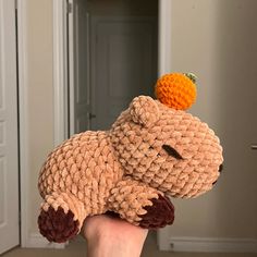 a hand holding a stuffed animal with an orange on its head