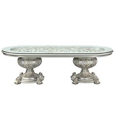 a glass table with two silver pedestals on each side and an ornate design on the top