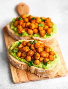 two pieces of bread with guacamole and chickpeas on top, sitting on a cutting board