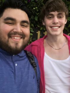 two young men standing next to each other in front of a green wall with flowers