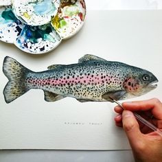 a painting of a rainbow colored fish being held by a person's hand with watercolor paints on it