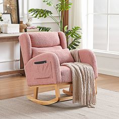 a pink rocking chair with a blanket on it in front of a mirror and potted plant