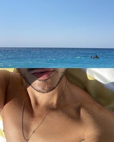 a shirtless man laying on top of a beach next to the ocean under a blue sky