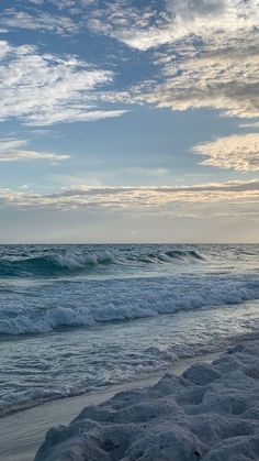 an ocean view with waves crashing on the shore and clouds in the sky above it