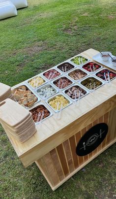 a wooden table topped with lots of trays filled with food on top of grass