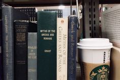 a cup of coffee sitting on top of a book shelf next to some books and other items