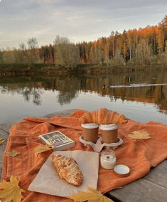 there is a pizza and coffee on the picnic table by the lake with autumn leaves