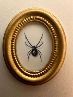 a close up of a spider in a gold frame on a white wall behind it