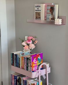 a book shelf filled with lots of books next to a vase full of pink flowers