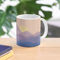 a coffee mug sitting on top of a wooden table next to a book and plant