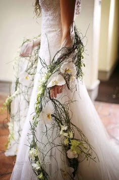 a woman in a wedding dress with flowers on the side and greenery around her waist