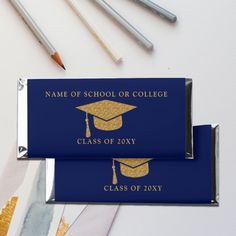 a blue graduation candy bar with gold foil on it and some pencils next to it