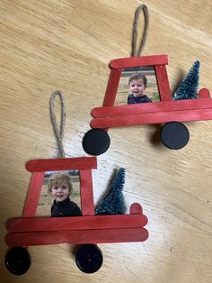 two red wooden toy cars are hanging from string on a wood table with blue christmas trees